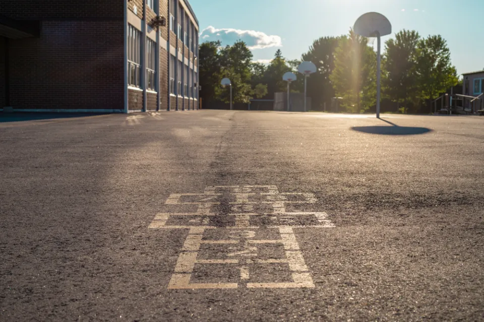 Hopscotch squares on concrete schoolyard with basketball hoop in background